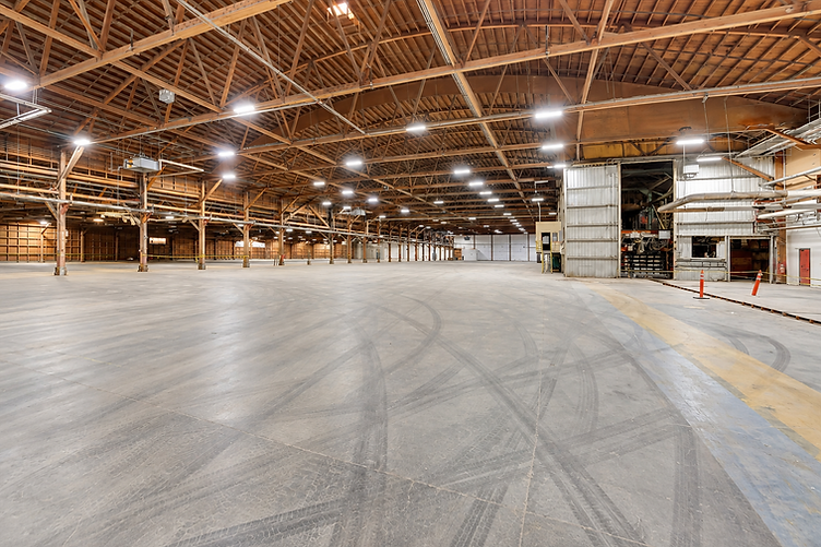 Interior of Soundstage 02 with high open-truss wooden ceiling, concrete floor with tire marks, and industrial sliding door