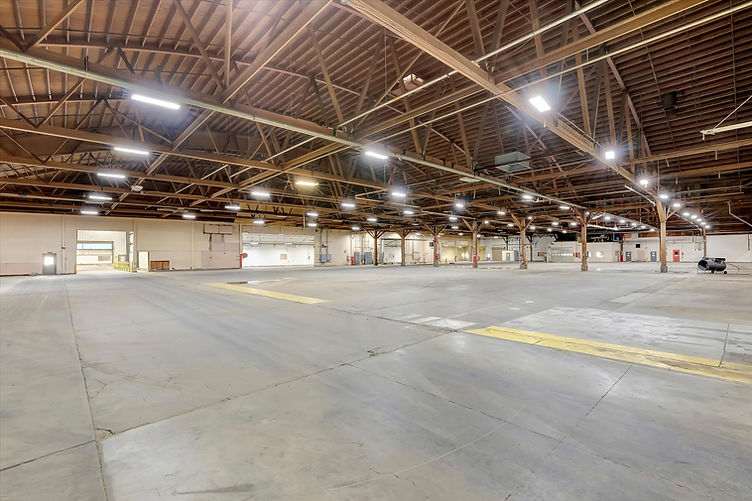 Wide-angle interior of Soundstage 04 with open concrete floor, exposed wooden trusses, and bay door openings