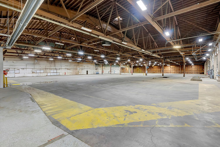 Interior view of Soundstage 05 with open-plan layout, wooden truss ceiling, and worn yellow floor markings