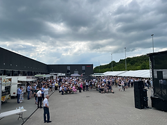 Udendørs event med højttalertårn, gæster og telte ved industribygning