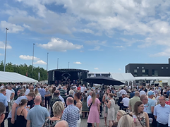 Udendørs scene med publikum samlet under telt på solrig dag