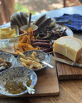 A charcuterie spread on wooden boards with biltong, droëwors, a wheel of cheese and blue-and-white bowls of preserves