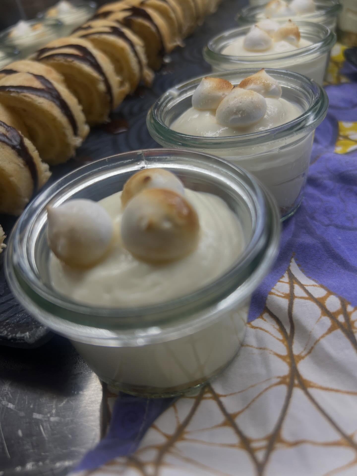 Small glass jars of creamy dessert topped with toasted meringue, beside a row of chocolate-drizzled biscuits