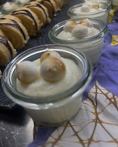 Small glass jars of creamy dessert topped with toasted meringue, beside a row of chocolate-drizzled biscuits