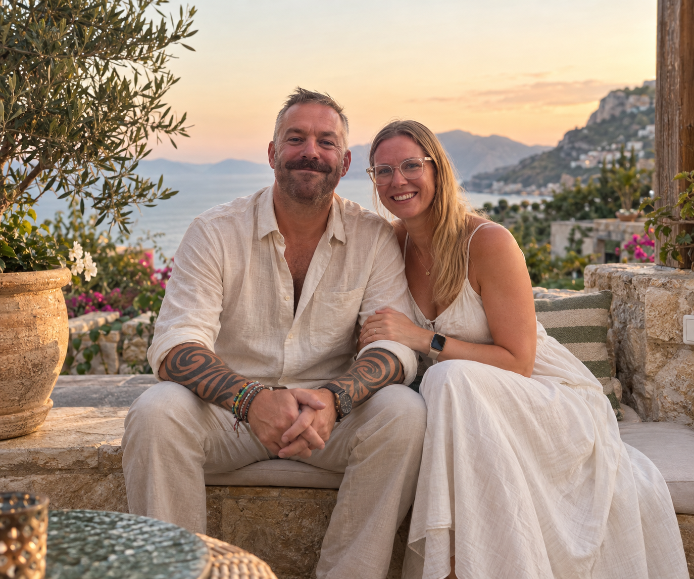 Lee and Lucy, the people behind Lose Your Way Travel, seated together on a terrace overlooking the coast at golden hour