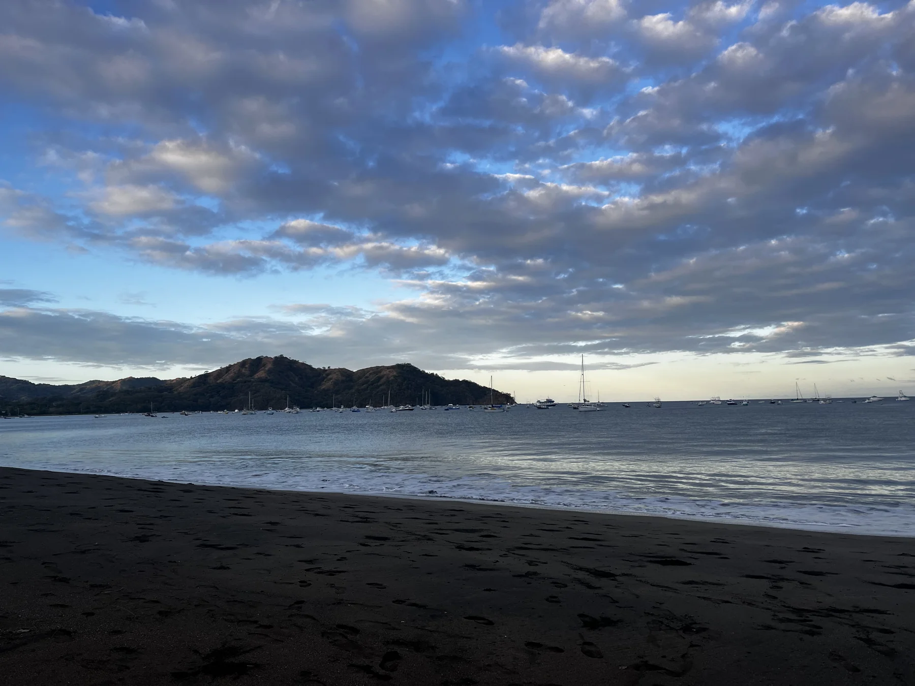 Sailboats anchored in a calm bay beneath a blue and cloudy sky
