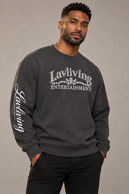 Man wearing a Shadow gray Lavliving Jeweled Crewneck with diamond arch chest branding and visible wearer-right sleeve script against a light neutral backdrop.