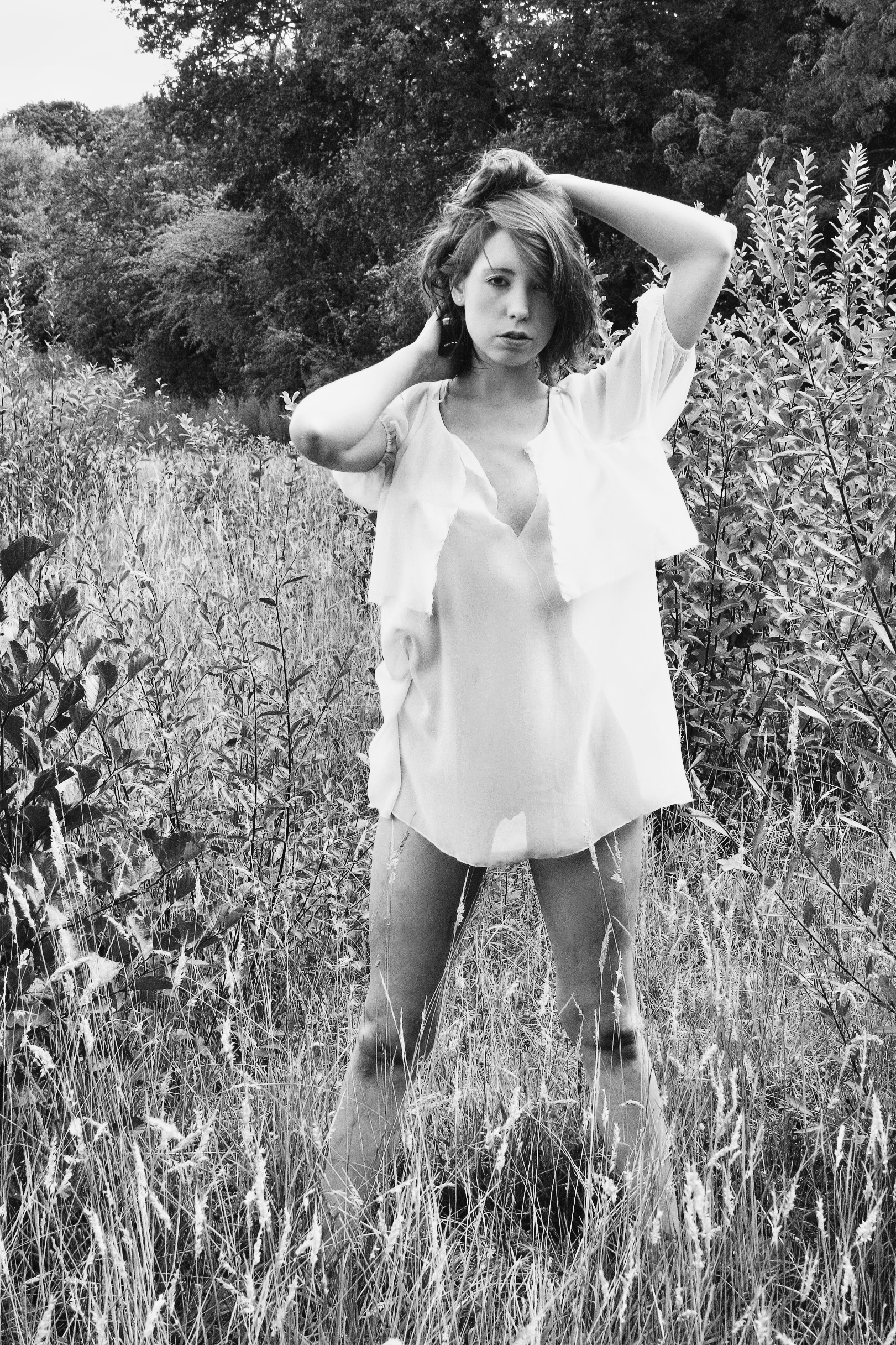 Woman in translucent blouse, arms raised, grassy field