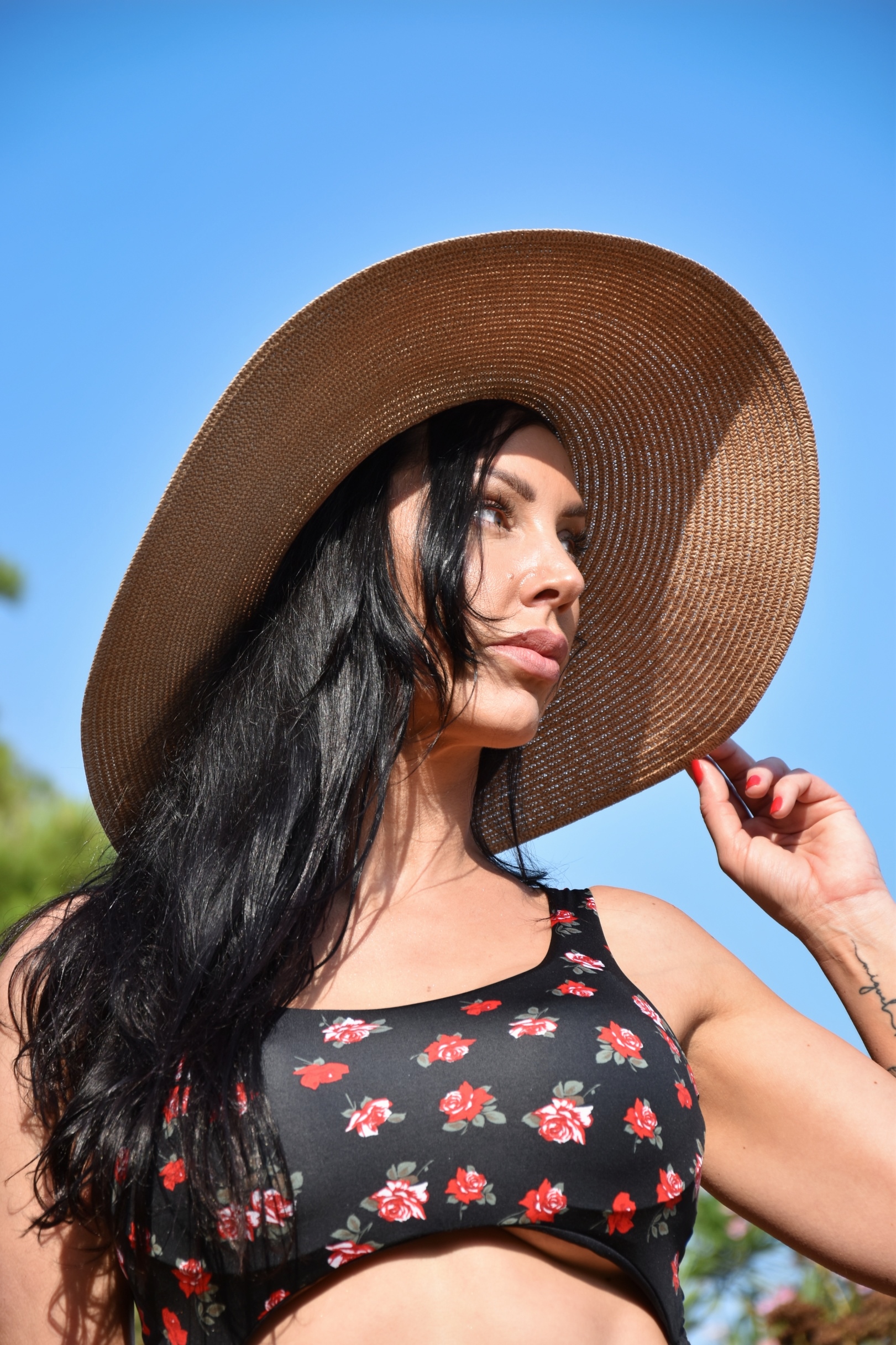 Woman in sun hat and floral top against blue sky