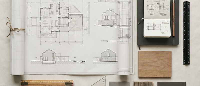 Overhead view of a planning table with site drawings, scale ruler and material samples