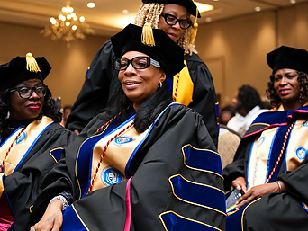 Three graduates in doctoral gowns with gold TIUA School of Business stoles and blue velvet sleeves at a university conferral celebration