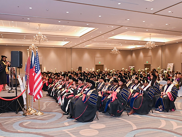 Conferral ceremony hall with speaker, flags, and graduates seated in regalia
