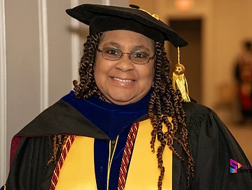 TIUAC graduate in doctoral tam and gown with a gold academic stole