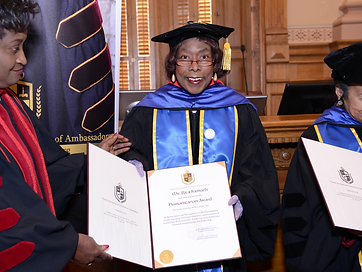 Three honorees in doctoral regalia presenting a humanitarian award certificate
