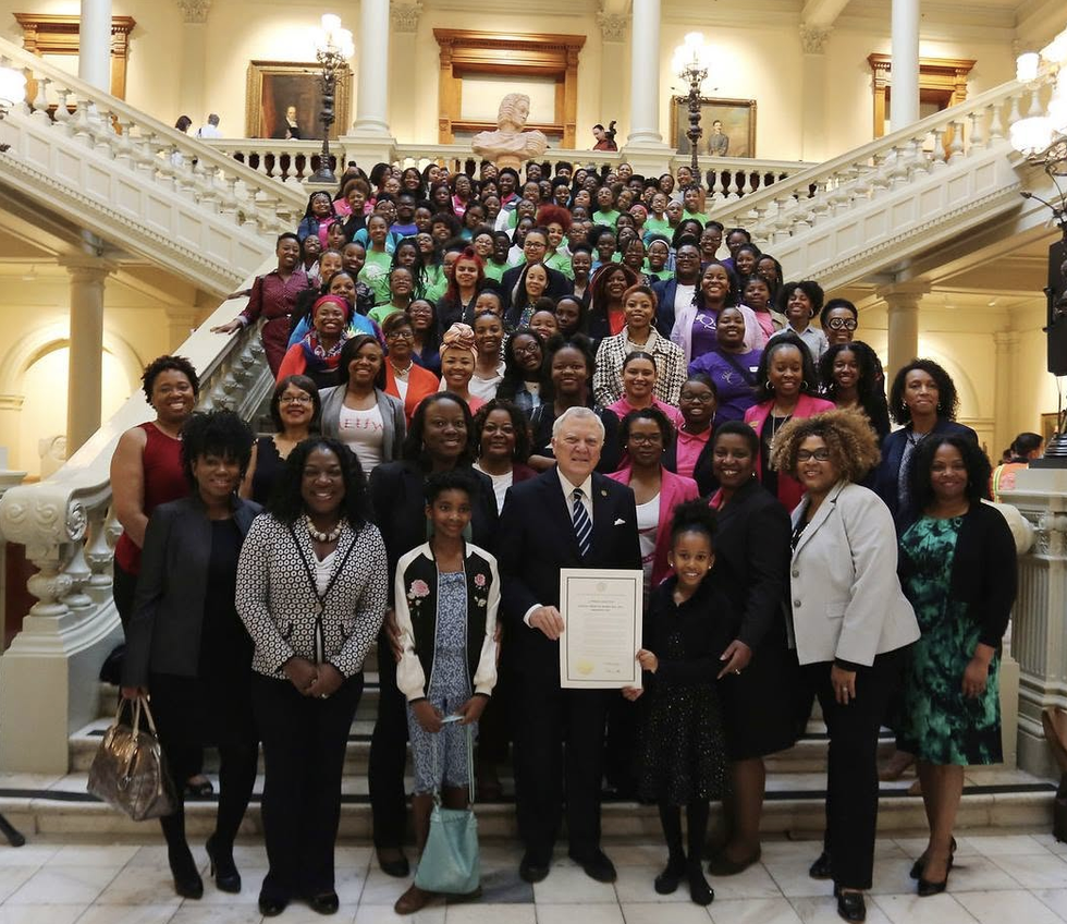 Group posing on the Georgia State Capitol staircase with a framed legislative resolution