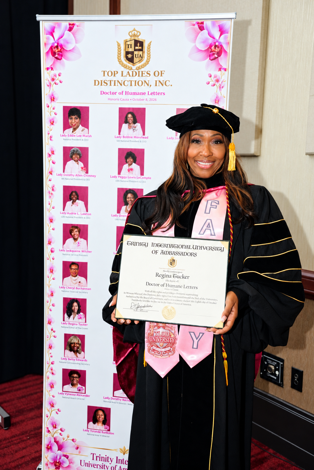 A Top Ladies of Distinction honoree in doctoral regalia holding her Doctor of Humane Letters diploma beside the TLOD member banner