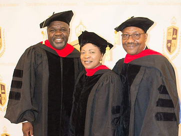 Three TIUAC doctoral graduates on the red carpet before the university crest backdrop