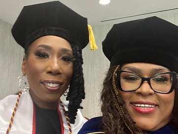 Two TIUAC doctoral honorees in tams and regalia celebrating together after the conferral