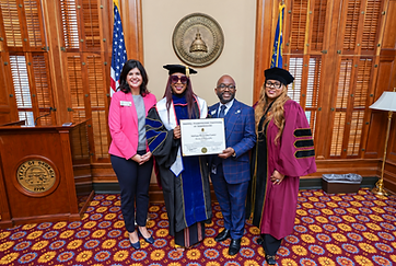 Dr. Adedayo Benjamins-Laniyi with colleagues on the floor of the Georgia General Assembly, holding a framed university recognition beside the Georgia State Seal