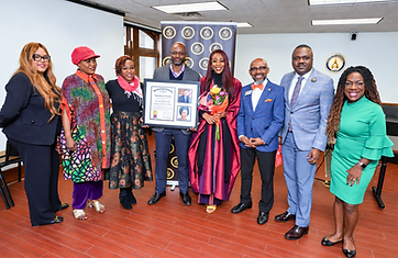 Dr. Adedayo Benjamins-Laniyi in maroon academic regalia with family, friends, and colleagues posing before a maroon and gold university banner