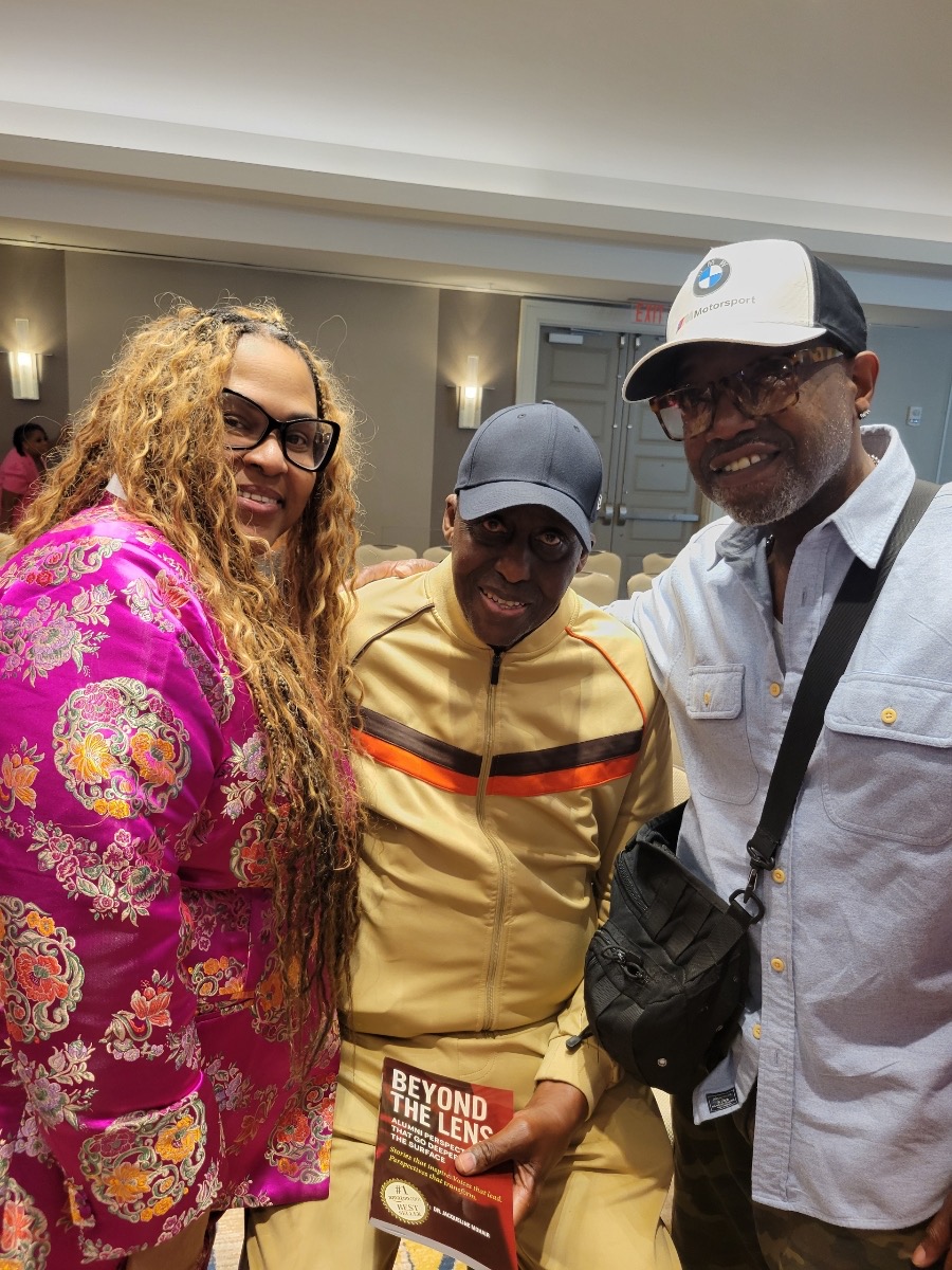 Three guests posing together with the Beyond the Lens book at the celebration
