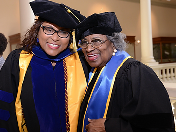 Two TIUAC graduates smiling together in caps and gowns with blue and gold stoles