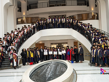 Large assembly of TIUAC graduates in caps and gowns on a grand staircase beside a fountain
