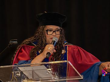 A speaker in academic regalia delivering the commencement address at the TIUAC lectern