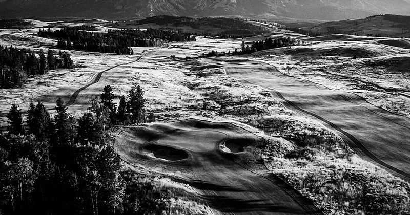 A Montana golf course at golden hour with mountain peaks in the distance