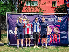 Cuatro personas posando frente al banner de Guesumoto Sports en el evento