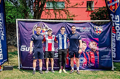 Cuatro personas posando frente al banner de Guesumoto Sports en el evento
