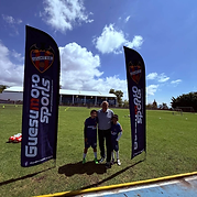 Adulto con dos jóvenes jugadores entre las banderas de Guesumoto Sports en el campo