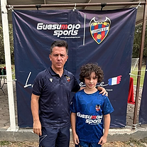 Jugador joven con entrenador posando frente al banner de Guesumoto Sports
