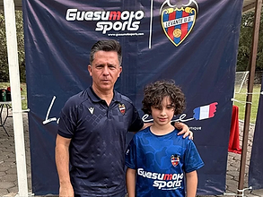 Jugador joven con entrenador posando frente al banner de Guesumoto Sports
