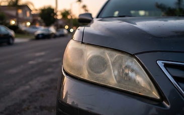 Close-up of a cloudy, yellowed car headlight at dusk on a Southern California street
