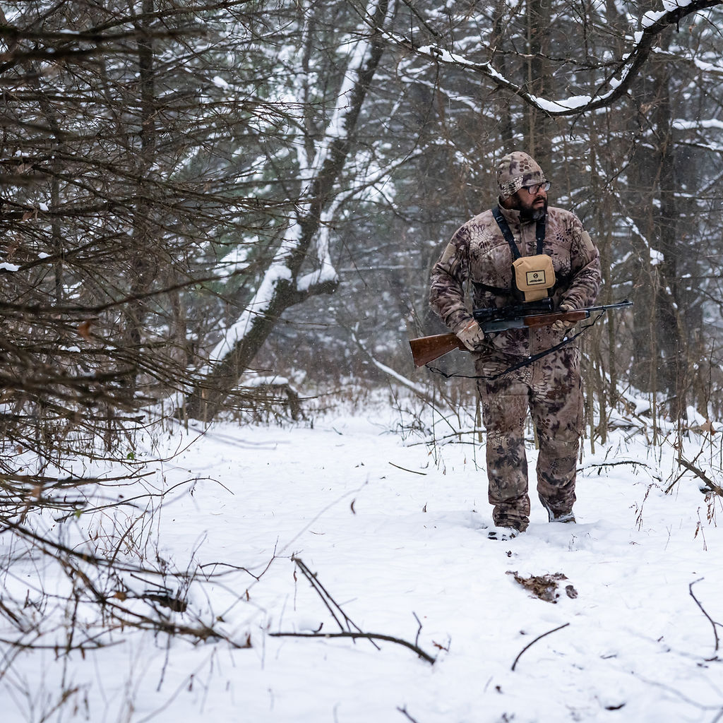 Hunter carrying a rifle through snow-covered woods — Overboard Media photography
