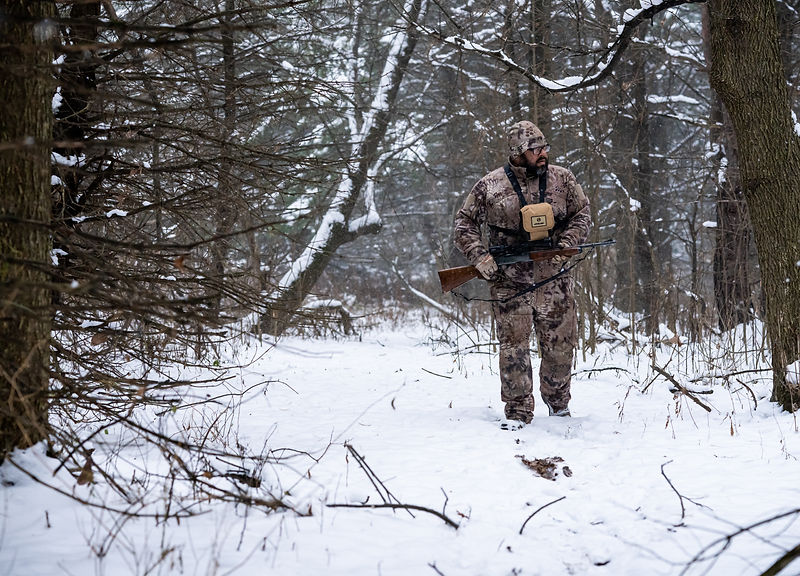 Hunter carrying a rifle through snow-covered woods — Overboard Media photography