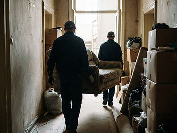 Entrümpelung: Zwei Mitarbeiter tragen ein Sofa aus einer Altbauwohnung, Kartons und Hausrat im Flur.