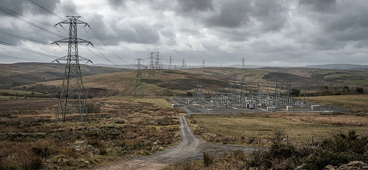 Transmission towers crossing low rolling hills with a switchyard in the distance