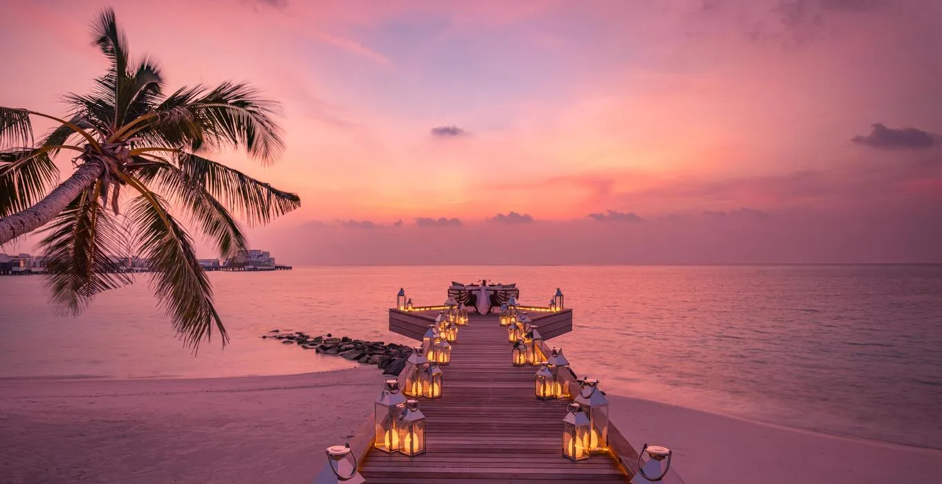 Candlelit jetty over a calm lagoon at sunset in the Maldives