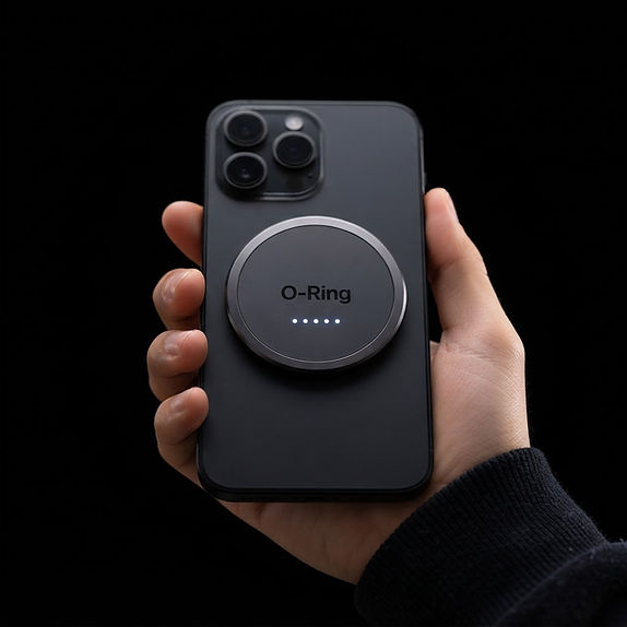 Hand holding a black smartphone with the O-Ring magnetic power ring attached to the back, five white charge dots illuminated, no cable