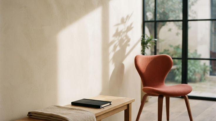 Quiet studio interior with warm plaster walls and a single coral chair