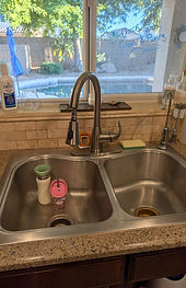 Older kitchen faucet at a double stainless sink before replacement