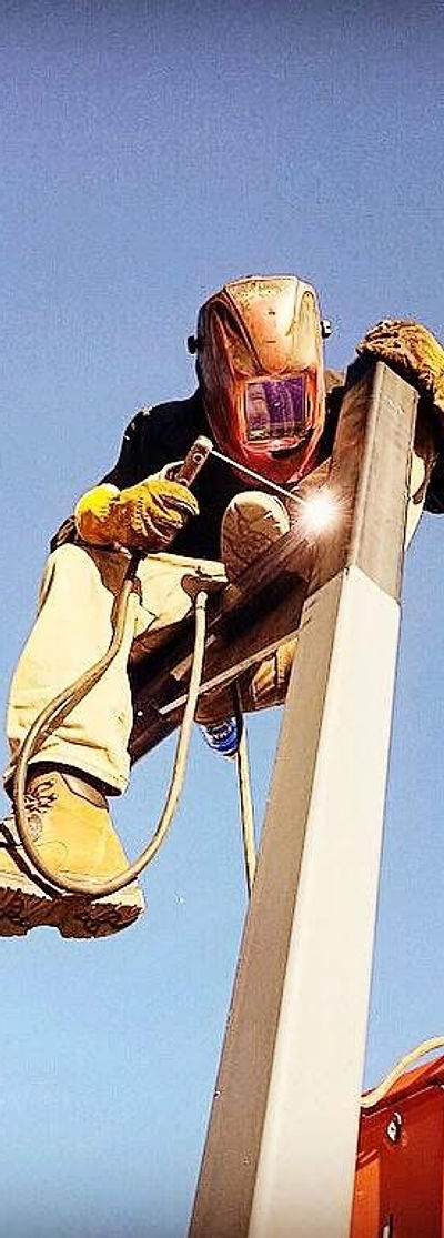 Chase Roncadori welding the top of a tall steel post on a field job