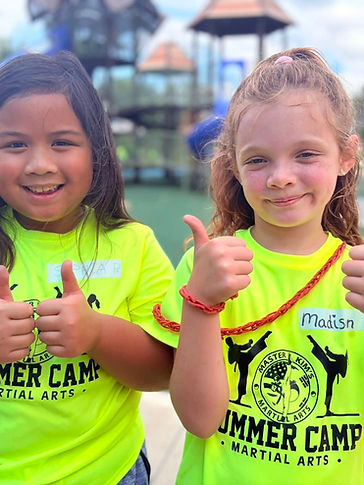 Two campers giving double thumbs up at the playground in neon camp shirts