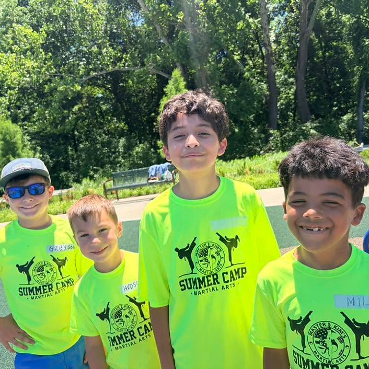 Four smiling kids in neon Master Kim's Summer Camp shirts at an outdoor playground
