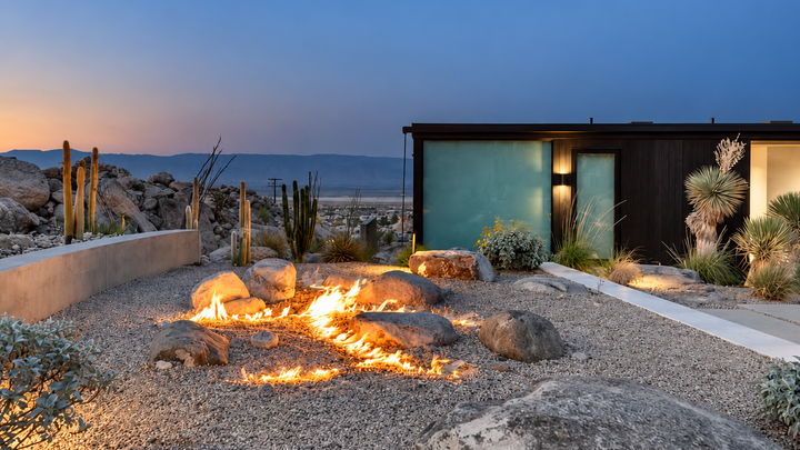 Fire pit integrated into gravel ground at twilight with desert rocks and a modern structure