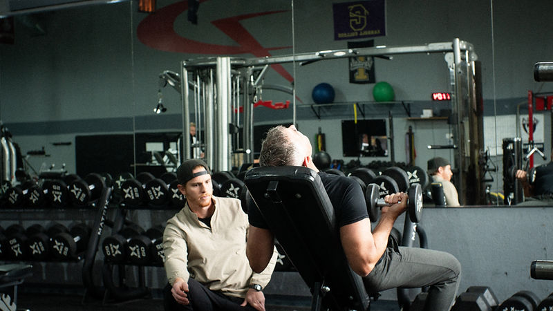 A trainer coaching a member through a dumbbell curl