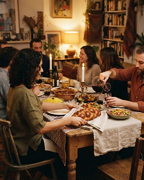 Friends and family seated around a Shabbat dinner table by lamplight, with challah, wine and shared dishes