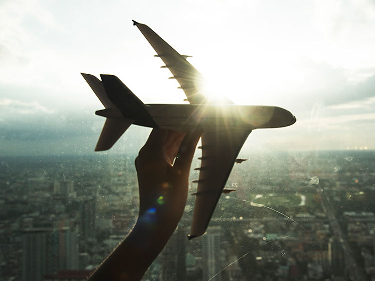Hand holding a model aircraft above a city skyline at sunrise